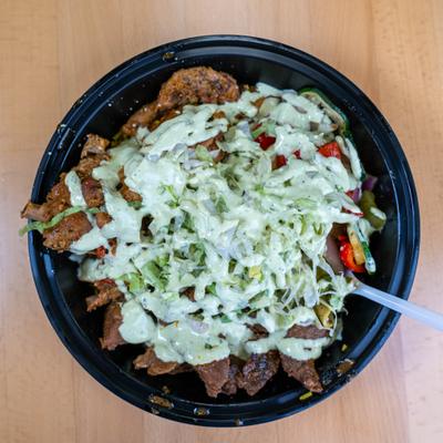 Bowl with shaved lettuce, grilled meat, vegetables, and creamy dressing drizzle.
