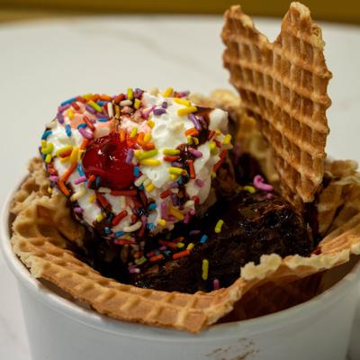 Brownie sundae with ice cream, rainbow sprinkles and a waffle bowl.