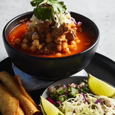 A bowl of pozole with crispy potato tacos, fresh cilantro, onion, and shredded cabbage.