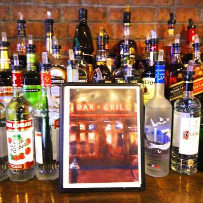 Liquor bottles surrounding a framed photo of a bar with neon signage.