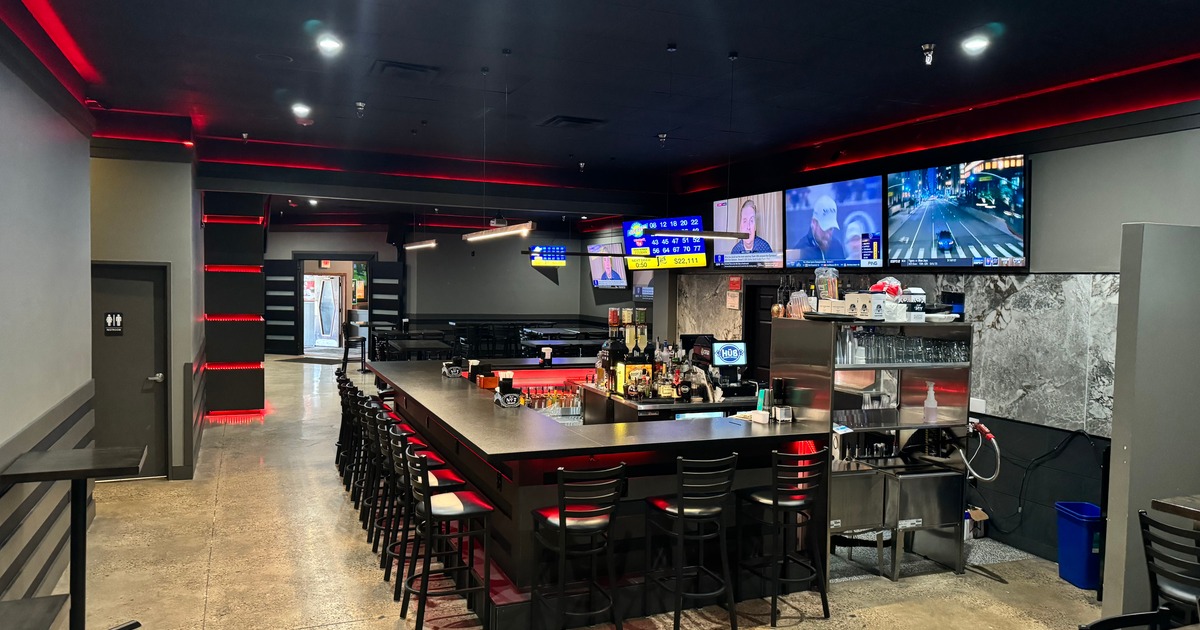 Interior of a bar with stools, TVs playing sports, glassware, and liquor bottles