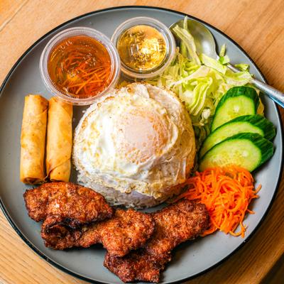 Lemongrass pork chops, served with crispy egg rolls, salad, rice, and a fried egg.