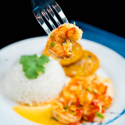 Fork with a bite of garlic shimp held over the plate with sides of rice and plantains.