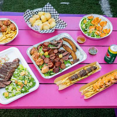 Assorted BBQ dishes in takeout containers arranged on a pink outdoor picnic table.