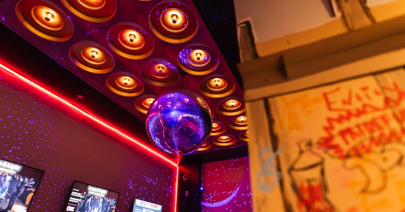 A purple disco ball hangs beneath a ceiling of warm, recessed lights