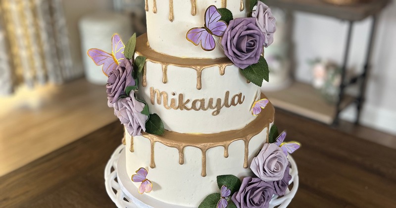 Three-tiered cake with purple flowers, butterflies, and gold icing drips