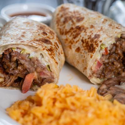 Close-up of a halved meat and bean burrito served with rice.