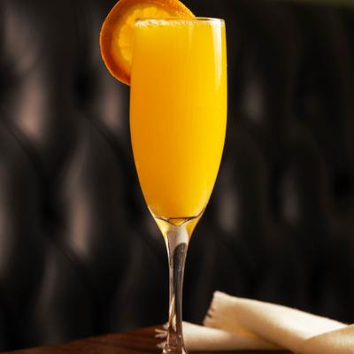 A tall flute glass filled with bright orange mimosa, garnished with an orange slice.