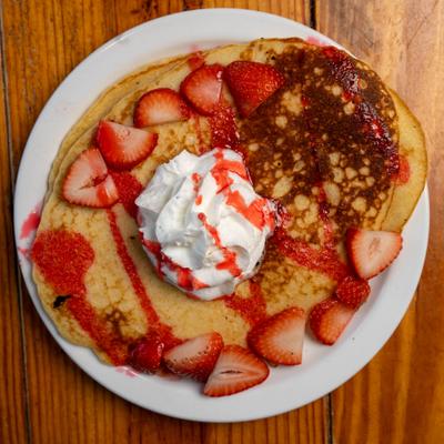 Pancakes topped with whipped cream, sliced fresh strawberries, and sweet red syrup.