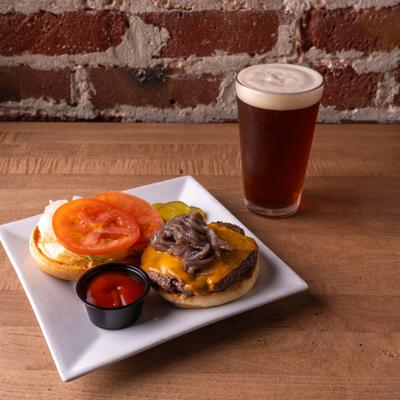 A cheeseburger served on a white plate alongside a glass of dark beer.