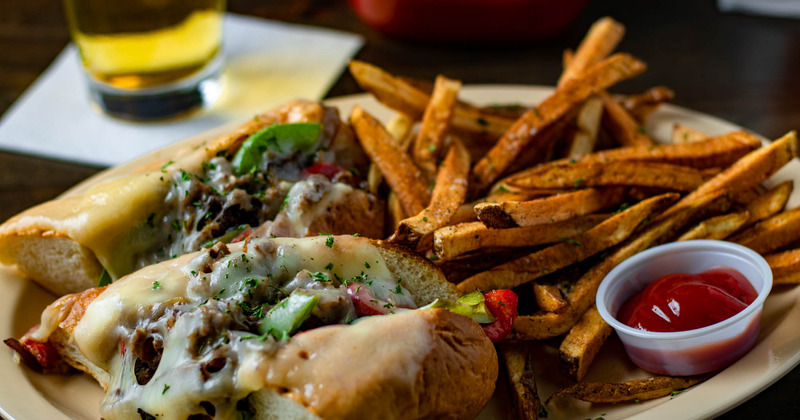 Philly cheese steak sandwich with fries and a sauce dip