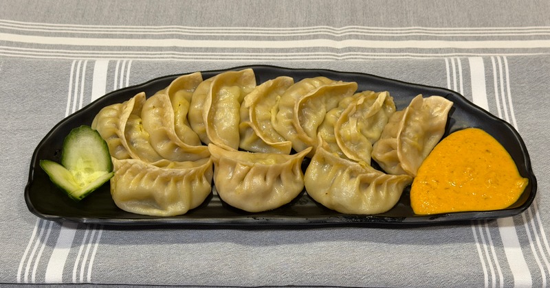 Steamed dumplings served on a plate with a dipping sauce and fresh garnish