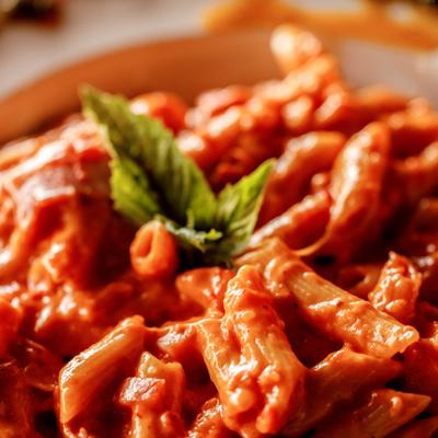 Penne alla vodka in creamy tomato sauce, garnished with basil, close-up.