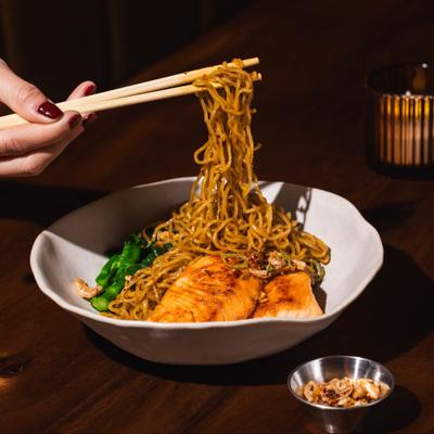 Person eating grilled salmon noodles.