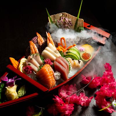 Sushi and sashimi boat with tuna, salmon, shrimp, scallop, roe, and dry ice fog.
