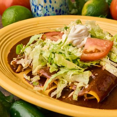 Enchiladas with mole sauce, topped with lettuce, tomatoes, and sour cream.