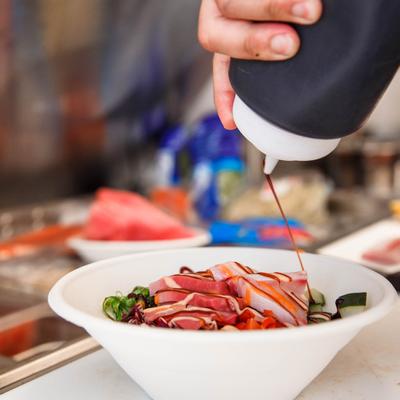 Person pouring teriyaki sauce on fish bowl