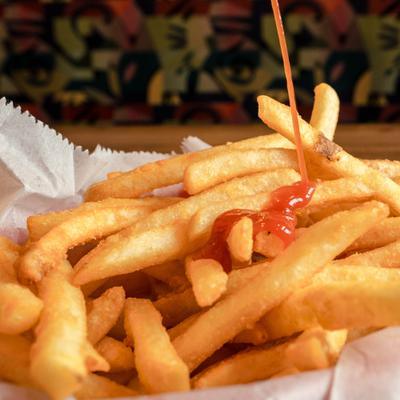 Portion of fries being drizzled with ketchup.