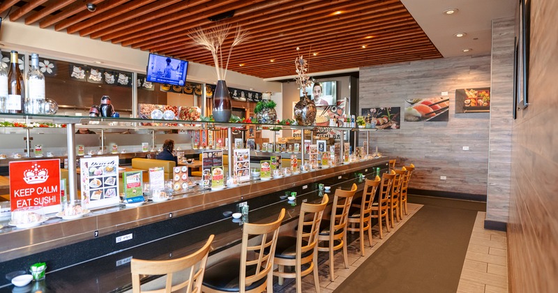 Cozy Japanese-style interior space, a long counter with wooden chairs along the rotating sushi belt