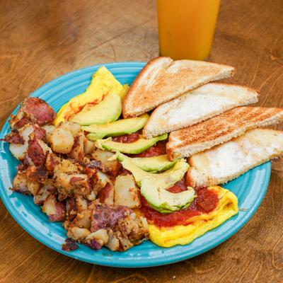 Salsa avocado omelet with sides, served with a glass of orange juice.