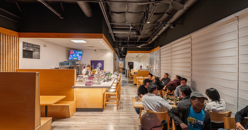 Modern sushi restaurant interior seating area with guests enjoying their food, and an open kitchen