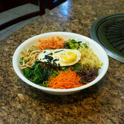Korean rice bowl topped with shredded vegetables and a fried egg.