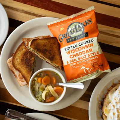 Turkey pesto melt sandwich served with a bag of chips and a bowl of soup.