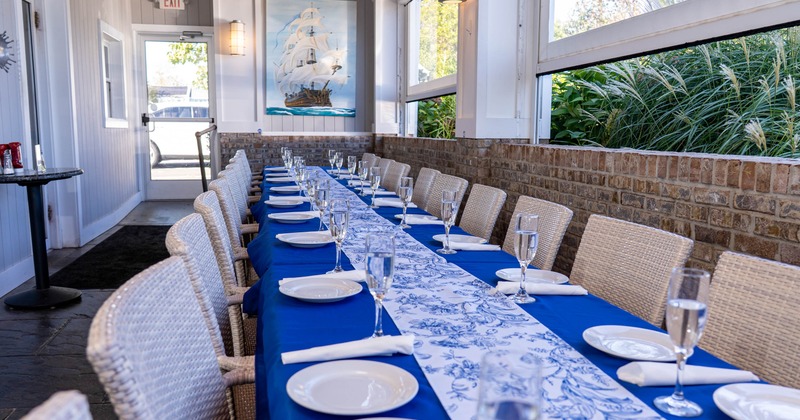 Long table setup for 20 plus people, blue table cloth, plastic wicker chairs, brick walls