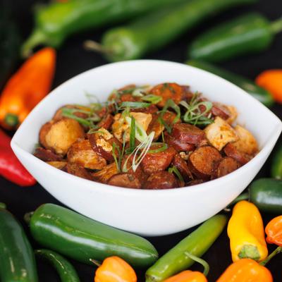 Sausage and chicken dish with scallions and herbs surrounded by fresh peppers.