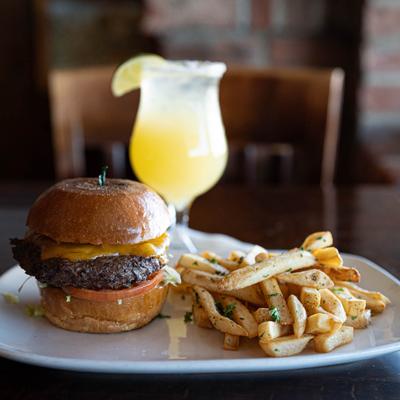 Signature burger with seasoned fries on a plate and a Margarita behind it.