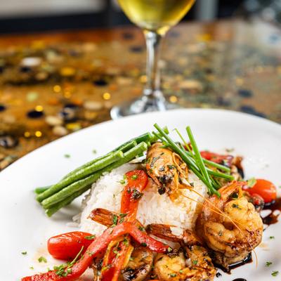 Grilled shrimp with rice, vegetables, and balsamic glaze, served with white wine.