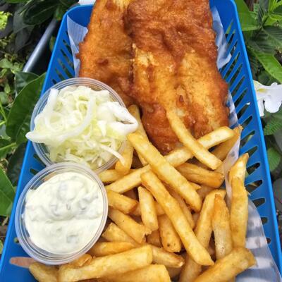 A blue basket of fish and chips with tartare sauce and slaw.