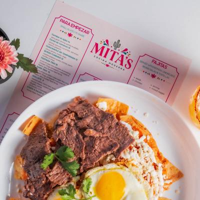 Chilaquiles topped with carne asada slices, fried eggs, and cheese.