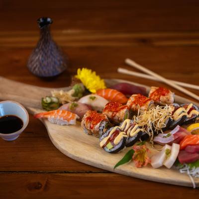 Assorted sushi rolls on a wooden board with a side of soy sauce.