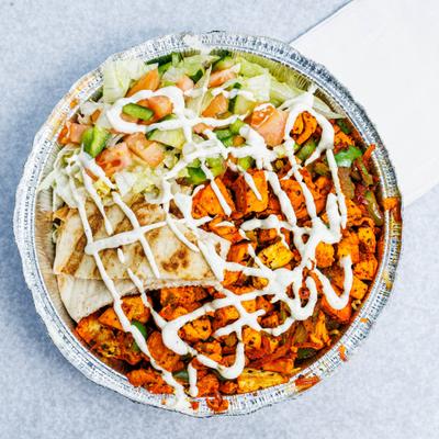 A foil bowl with spicy grilled chicken, pita and salad drizzled with sauce.