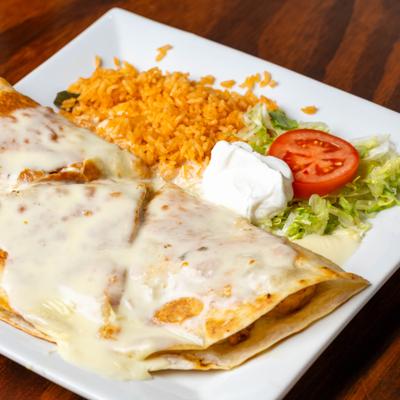 Quesadillas topped with cheese sauce, served with rice and sour cream.