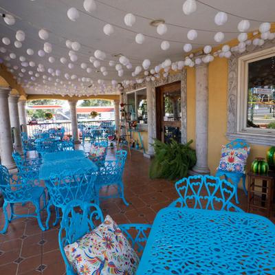 Covered patio featuring vibrant turquoise metal chairs and tables and a string of globe lights.
