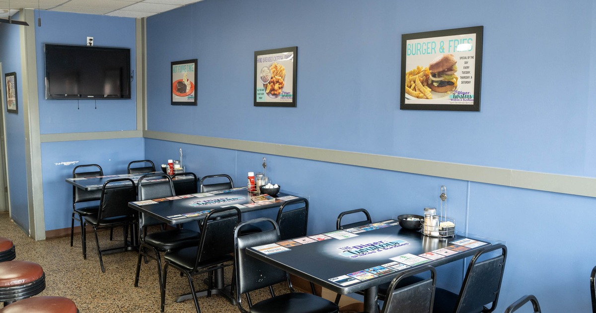 Interior, casual diner with black tables and chairs, light blue walls, and a mounted flat-screen TV