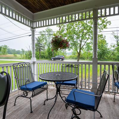 Covered porch with black metal table and chairs, blue cushions, and a view of a road and trees.