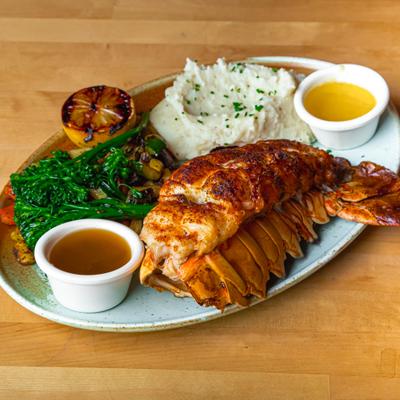 Lobster tail is served with mashed potatoes, broccolini, and two dipping sauces.