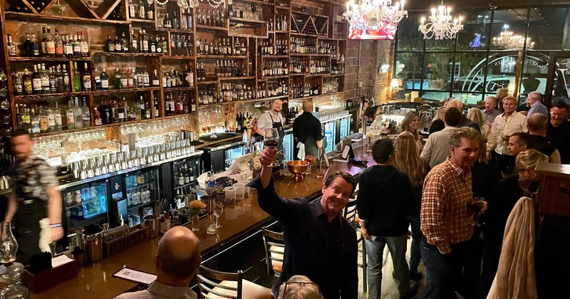 Guests standing in the bar area with a long counter and crystal chandeliers