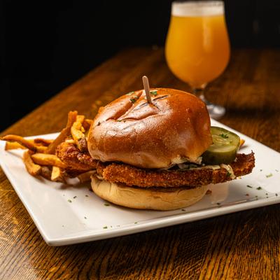 Fried chicken sandwich with pickles, served with fries and a glass of beer.