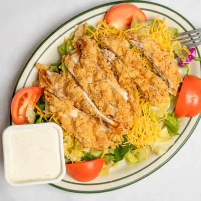 Crispy chicken salad with lettuce, tomatoes, shredded cheese, and a cup of dressing.