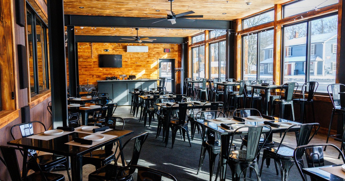 Bright restaurant interior with wooden ceiling, black tables and metal chairs, and large windows