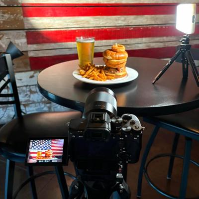 Burger, fries and a beer on a table with a digital camera in the foreground.