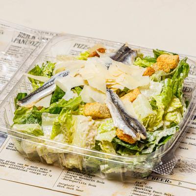 Caesar Salad topped with anchovies and shaved parmesan in take-away container.