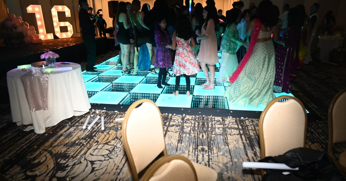 A lively sweet sixteen party with people dancing on a LED checkered floor