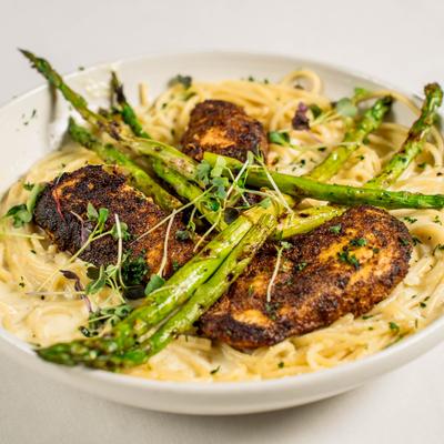 Alfredo pasta with creamy sauce topped with blackened chicken, grilled asparagus and herbs.