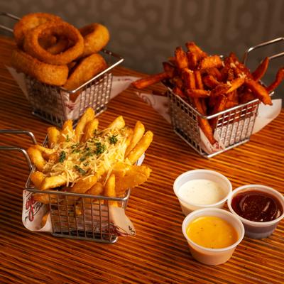 Baskets of sweet potato fries, cheese fries, and onion rings served with dipping sauces.