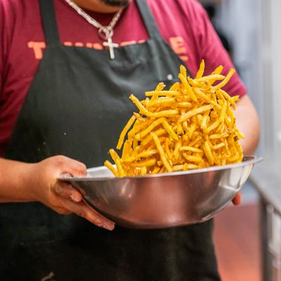 A chef tossing fries in a large bowl.